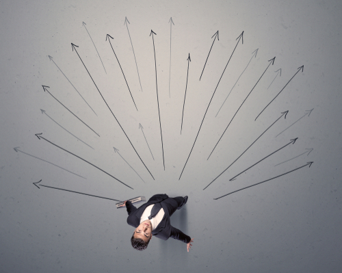 Young contemplating businessman stands in front of grey arrows 