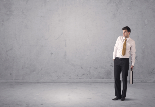A surprised young sales person in elegant suit standing in empty urban environment with grey concrete wall background concept