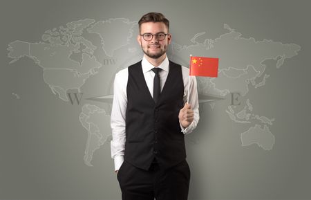 Cheerful businessman standing in front of a map with flag on his hand
