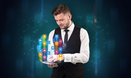 Elegant businessman holding tablet with hologram application icons and symbols above
