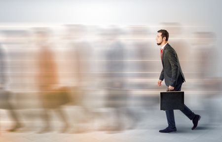 Young businessman with briefcase hurry up on a crowded street with blurred people around
