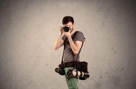 A professional male photographer with belt holding a camera and taking photos in front of clear grey urban wall background concept