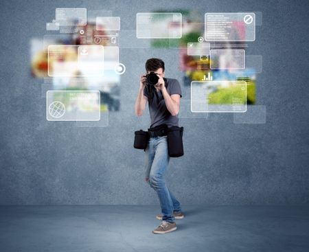 A young professional male photographer holding cameras and taking pictures in front of a blue wall with pictures, icons, text information concept