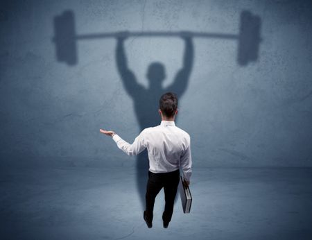 A confident young elegant salesman with briefcase facing a wall, looking at his strong, weight lifting shadow concept