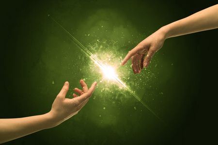 Two naked male hands about to touch, lighting the spark with modest explosion in front of green background concept