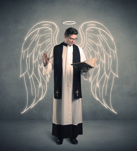 A young male priest with drawn large angel wings standing with the holy bible in his hands concept.