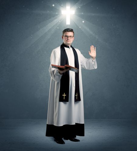 young-caucasian-priest-deep-faith-blessing-794267665 A young caucasian priest with deep faith blessing with the holy bible in his hand in front of blue wall background with illustrated glowing cross concept.