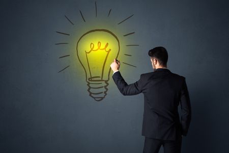 Young businessman in black suit standing in front of a drawn yellow lightbulb 