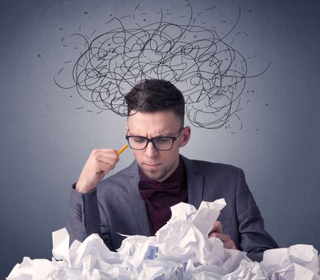 Young businessman sitting behind crumpled paper with scribbles over his head