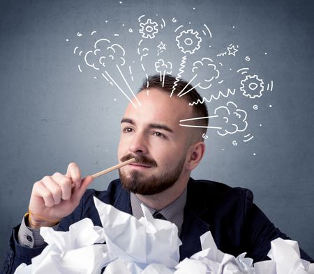 Young businessman sitting behind crumpled paper with drawings of gears and steam over his head
