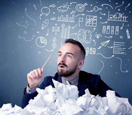 Young businessman sitting behind crumpled paper with mixed drawings over his head