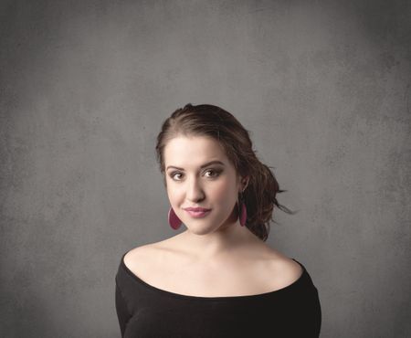 A pretty young teenage girl standing in front of a grey clear empty urban wall background concept while making funny faces.