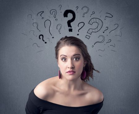 A pretty teenage girl standing confused in front of grey wall background with drawn question marks concept.