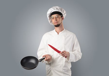 Young bearded cook portrait with kitchen tools and empty wallpaper 
