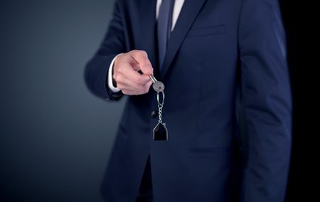 Young businessman hand over keys with empty dark background
