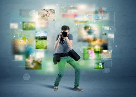 A young amateur photographer with professional camera equipment taking picture in front of blue wall full of faded pictures and glowing lights concept