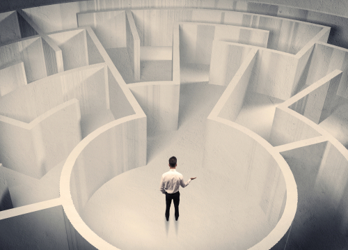 A confused businessman standing in the center of a maze surrounded with walls of the labyrinth