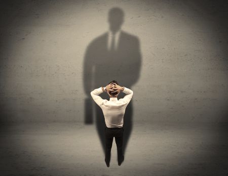 A young beginner salesman standing in front of a wall, facing his shadow as his boss or a successful businessman he lloks up to concept