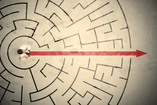 Business person standing in the middle of a circular maze with red arrow