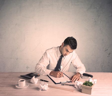 A young office worker sitting at desk working with keyboard, papers, highliter in front of empty clear background wall concept