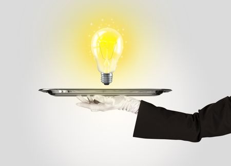 Serving a bright business idea concept using a bulb with bright sparkling warm yellow light presented on a silver plate