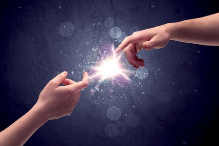 Two male hands reaching towards each other, almost touching with fingers, lighting spark in galaxy background concept