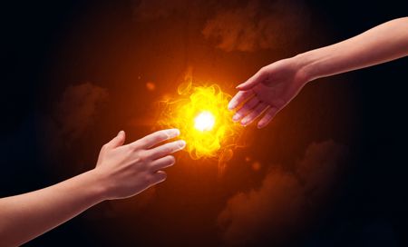 Two naked male hands about to touch, lighting a bright flame with smoke in red sky background concept