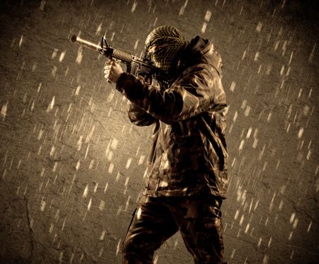 Portrait of dangerous heavily armed terrorist soldier with mask on grungy rainy background 