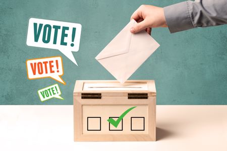 A hand placing a voting slip into a ballot box