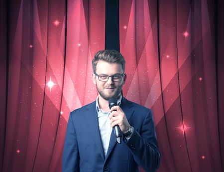 Businessman speaking into microphone with red curtain behind him 