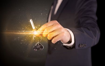 Businessman hand  over shiny keys in dark suit with dark background
