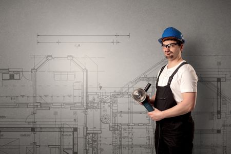 Worker standing with tool in his hand in front of technical drawings.