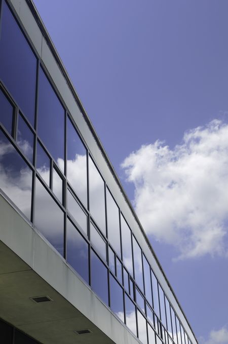 Campus reflections: Windows of long university building reflect white cloud in blue  sky