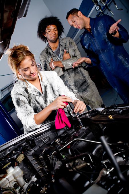 Female mechanic working on the hood of a car while colleagues watch