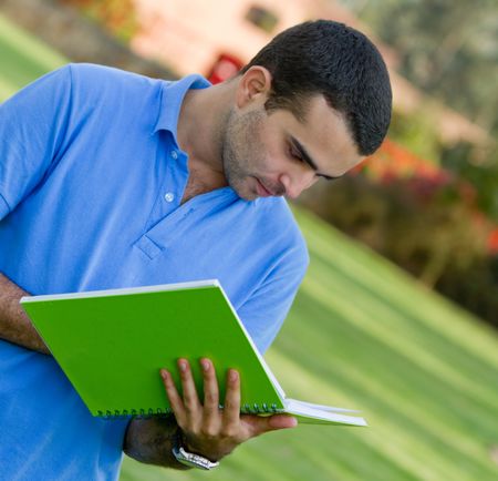 Male student with a notebook outdoors and smiling