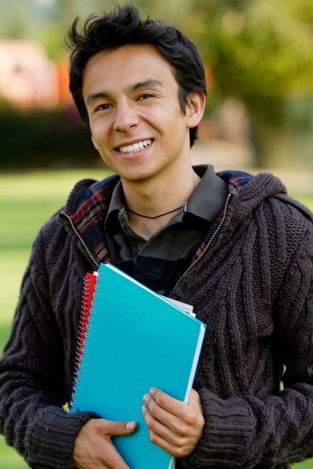 Male student with a notebook outdoors and smiling