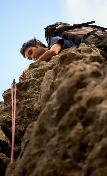 male climber on top of a rock setting up his grip and ropes