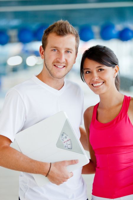 Couple at the gym holding a scale - lose weight concepts