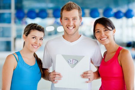 Women at the gym with their trainer holding a scale - lose weight