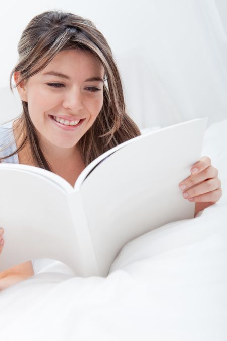 Beautiful young woman reading a book in bed