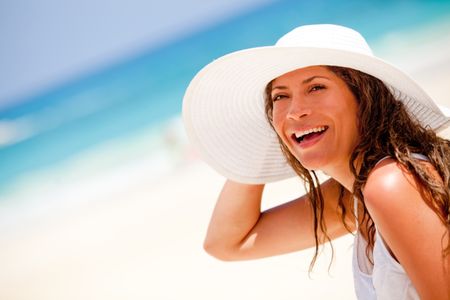 Happy woman at the beach wearing a hat on a summer day