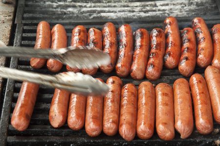 Picnic at a glance: Pair of tongs reaching -- with motion blur -- toward shiny hot dogs on outdoor grill