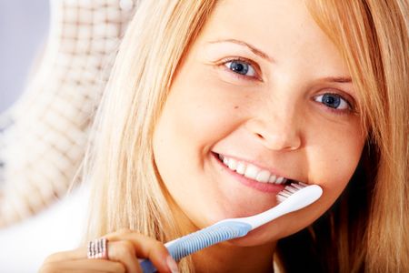 beautiful woman brushing her teeth by a mirror