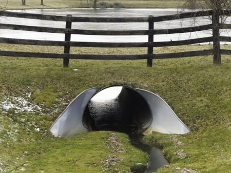 Landscaper's solution to prevent flooding from rain or snowmelt: Steel culvert with collar by wooden fence near pond in mid December