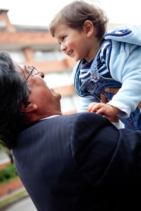 Young grandfather holding a child in the air and smiling - outdoors
