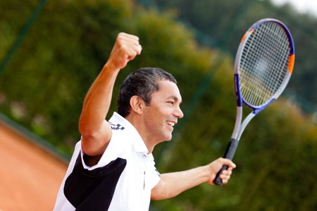 Man winning at tennis with arms up and holding a racket