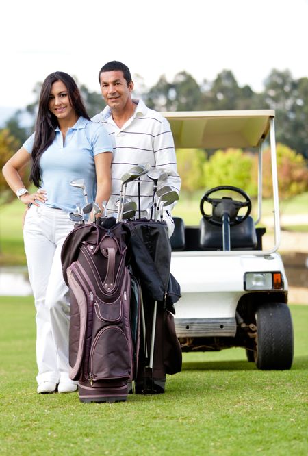 Couple playing golf posing with a cart and a bag smiling