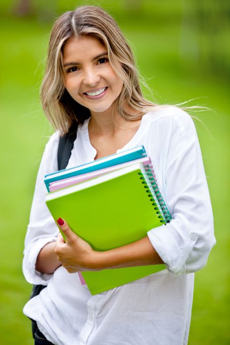 Gorgeous female student holding notebooks outdoors