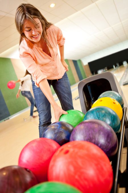 Casual woman picking up a bowling ball