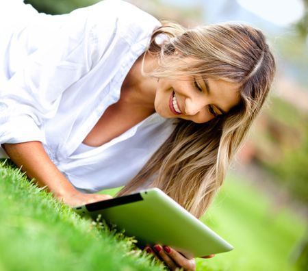 Woman lying outdoors with a tablet computer and smiling